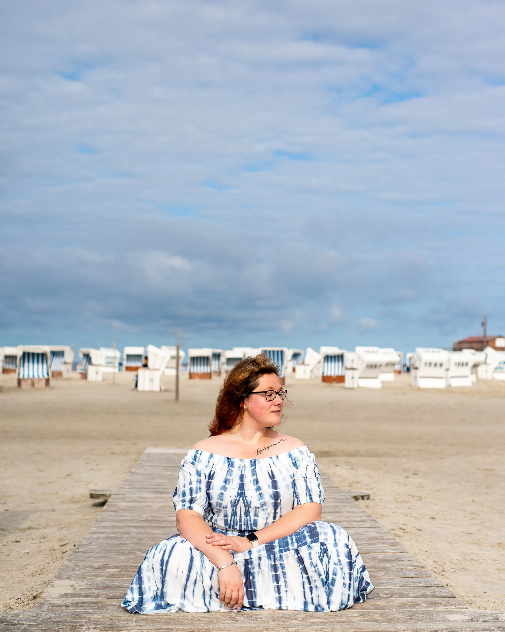 Portraitshooting am Strand: sitzend auf dem Steg vor einer Reihe Strandkörbe