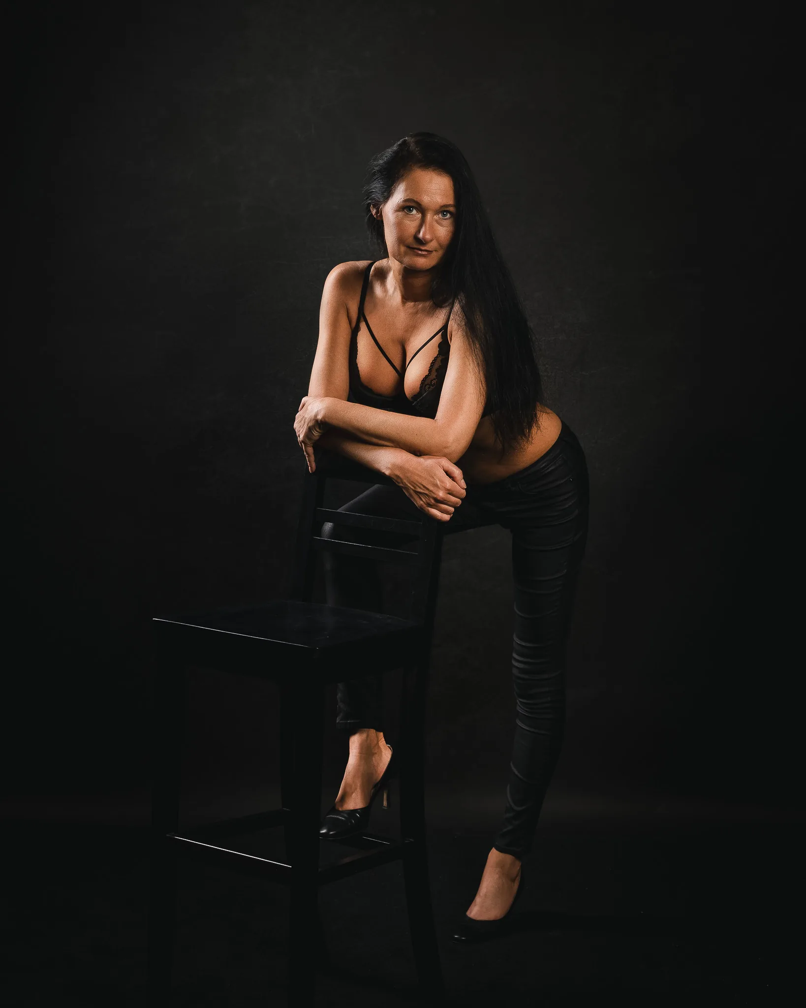 Sinnliche Fotografie: Ganzkörper-Portrait in schwarzer Spitzenwäsche, an einen Stuhl gelehnt, im dunklen Studio