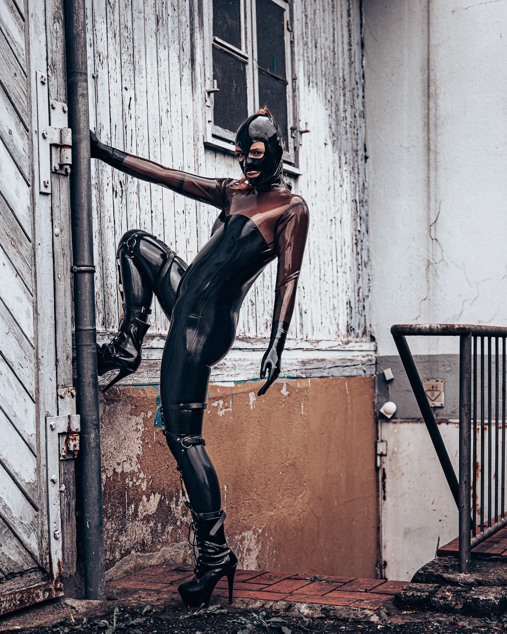 Sinnliche Fotografie im Freien: Latex-Catsuit und Maske an einer alten Hauswand