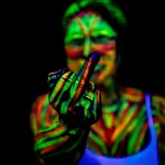 Frau die mit UV-Farbe bemalt wurde und eine Geste in Richtung Kamera macht