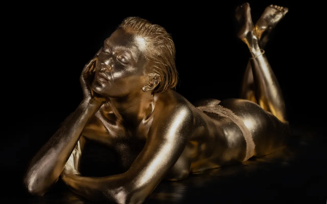 Frau mit Goldüberzug, die auf dem Bauch liegt mit geschlossenen Augen - Marcus Beelitz – Fotograf
